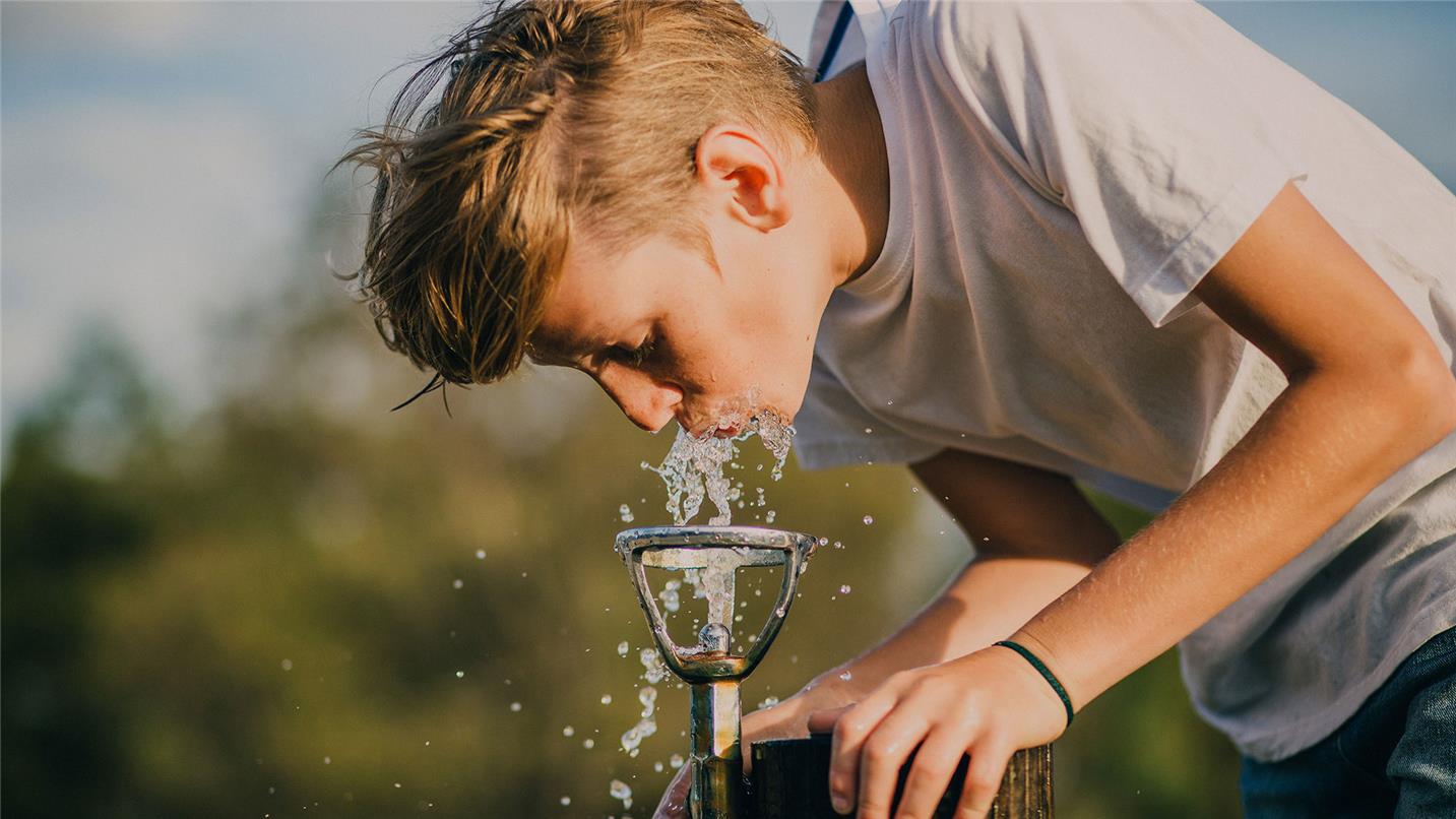 young guy drinking water from a little fountain young guy drinking water from a little fountain