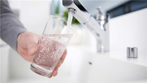 Personne remplissant un verre d’eau au robinet d'une cuisine