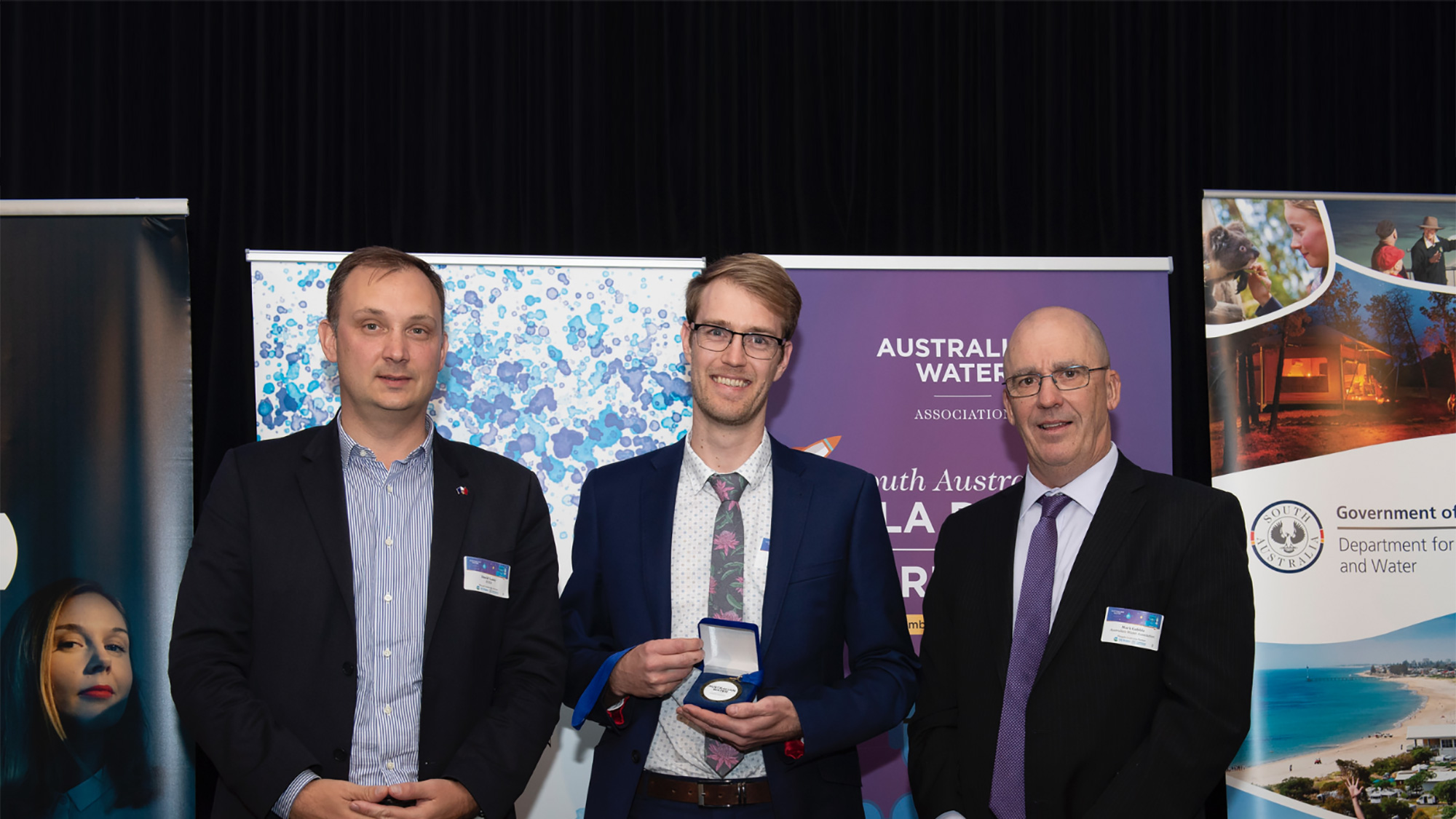 three men standing with a prize